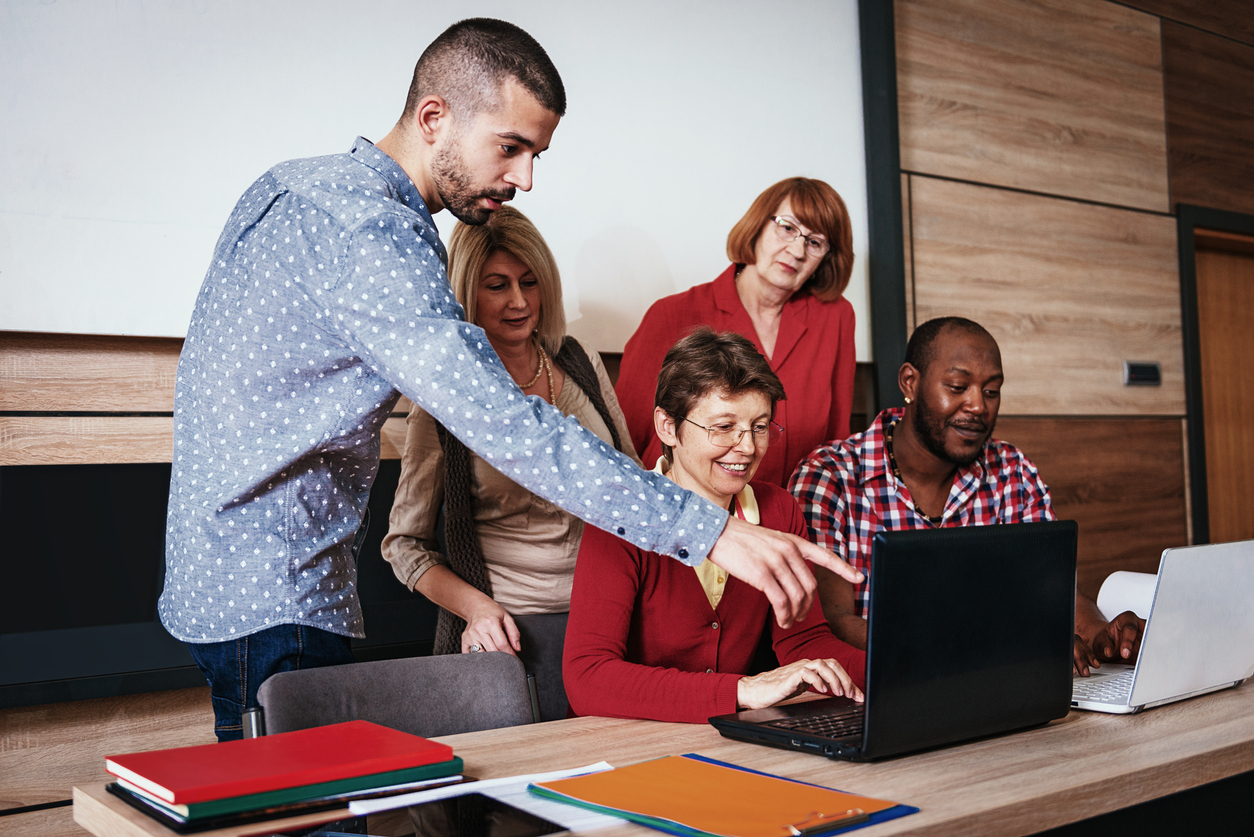 man pointing at computer screen, guiding a diverse team of educators